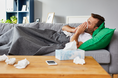 sick man blowing his nose into a tissue while lying on the couch
