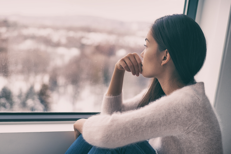 woman with seasonal affective disorder looking out window on dreary winter day