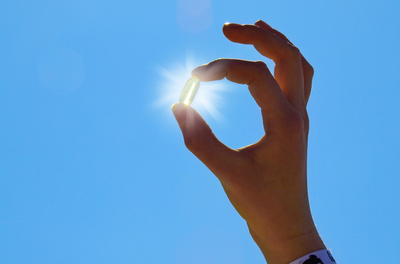 vitamin D supplement held up in front of the sun in a blue sky