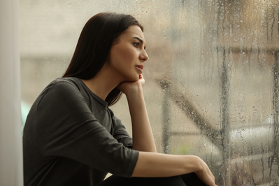 woman looking out window at dark, rainy day