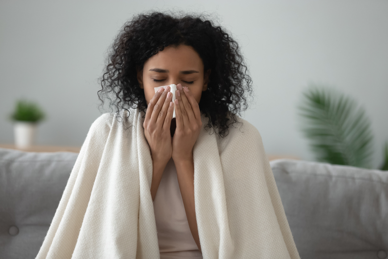 young woman covered with blanket blowing nose