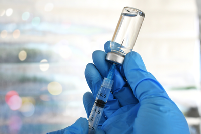 gloved hands filling syringe with vaccine from vial