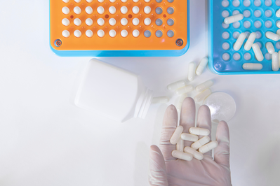 gloved hand holding white pills next to pill filling machine