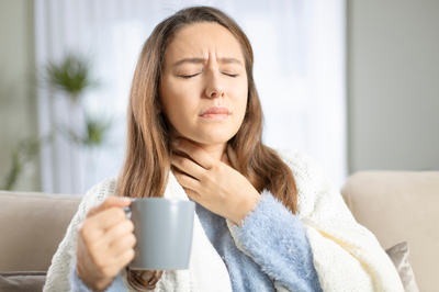 woman with sore throat holding neck and cup of tea