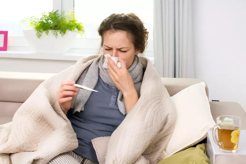 sick woman looking at a thermometer while holding tissue to her nose