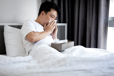 man blowing nose into tissue while in bed